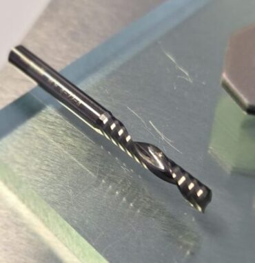 Close-up of a shiny twist drill bit resting on a scratched metal work surface.