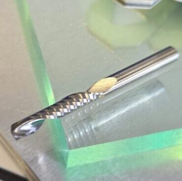 Close-up of a twisted metal drill bit on a shiny metal surface with a green-tinted display in the background.