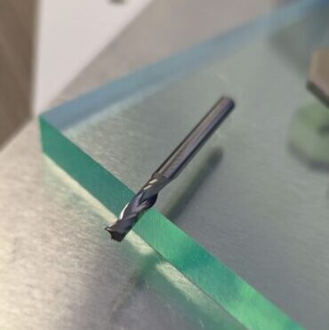 Close-up of a twist drill bit resting on a shiny metal surface with a green edge.