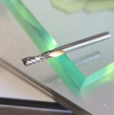 Close-up of a silver twist drill bit resting on a glass table, with a green edge glow in the background