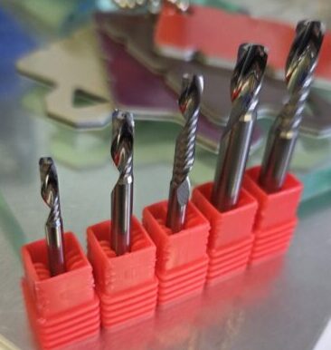 Six twist drill bits in red plastic holders arranged in a row on a metallic workspace surface