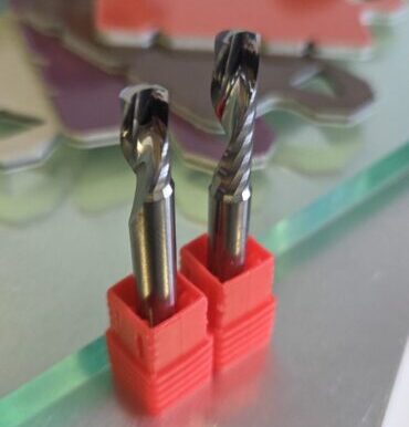 Two twist drill bits standing upright in red holders on a metal work surface in a workshop.