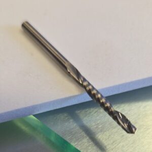 Close-up of a metal twist drill bit resting on a white surface.