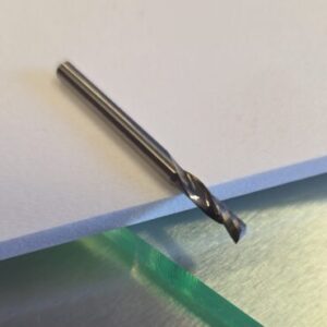 Twist drill bit lying on a white sheet atop a metal work surface.
