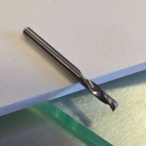 Close-up of a silver twist drill bit resting on a white sheet of paper atop a stainless steel work surface.