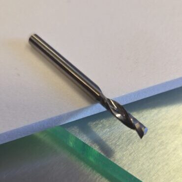 Close-up of a silver twist drill bit resting on a white sheet of paper atop a stainless steel work surface.