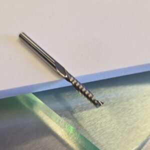 Close-up of a metal twist drill bit lying on a white sheet atop a stainless-steel work surface.